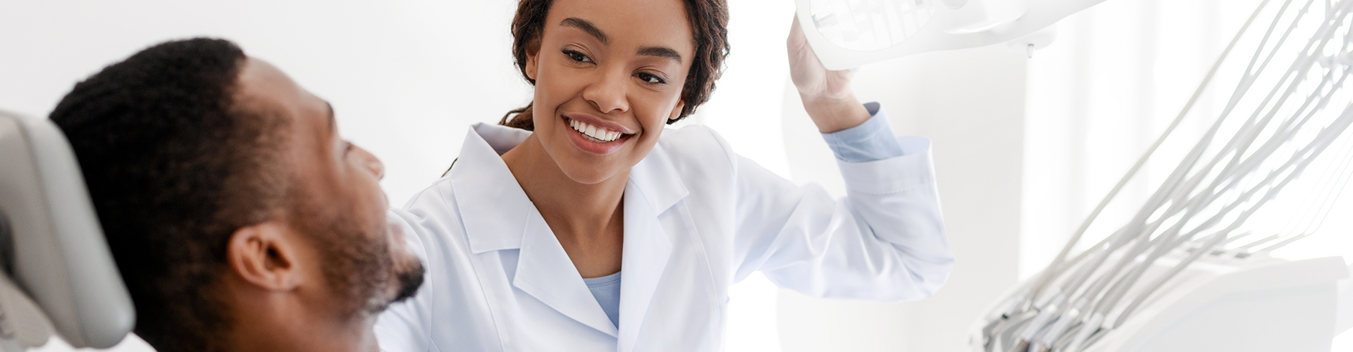 dentist positioning light on man's smile in dental chair