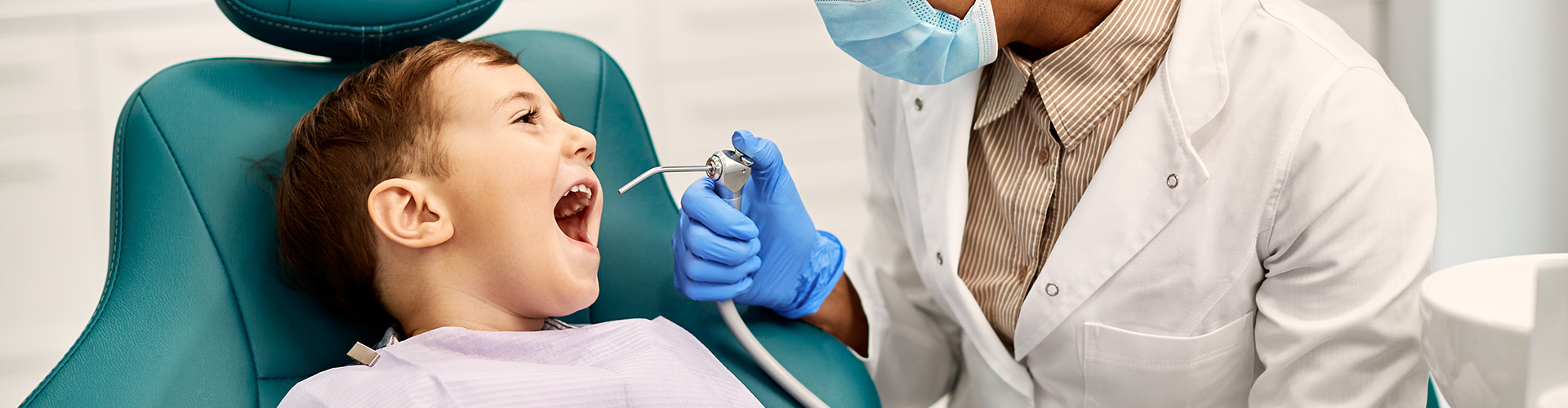 dentist holding dental tool at kid's mouth in dental chair