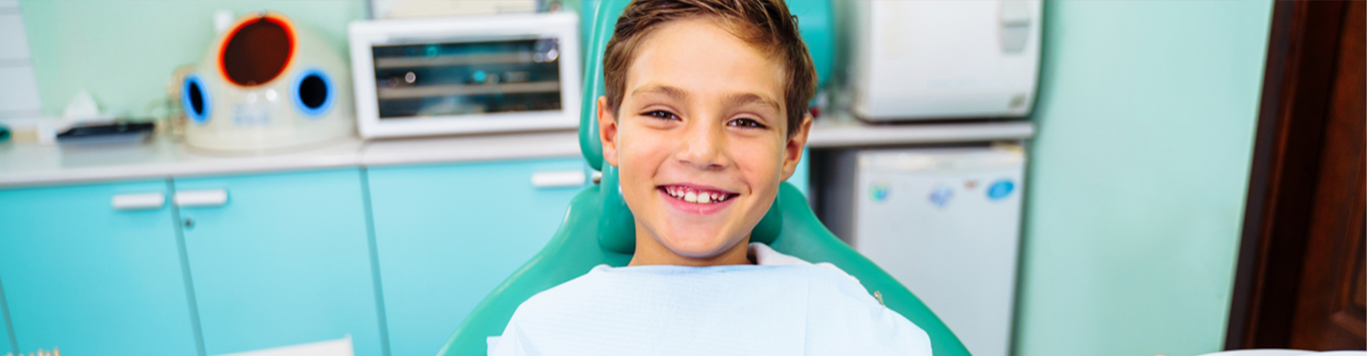 Kid in dentist chair smiling with two thumbs up