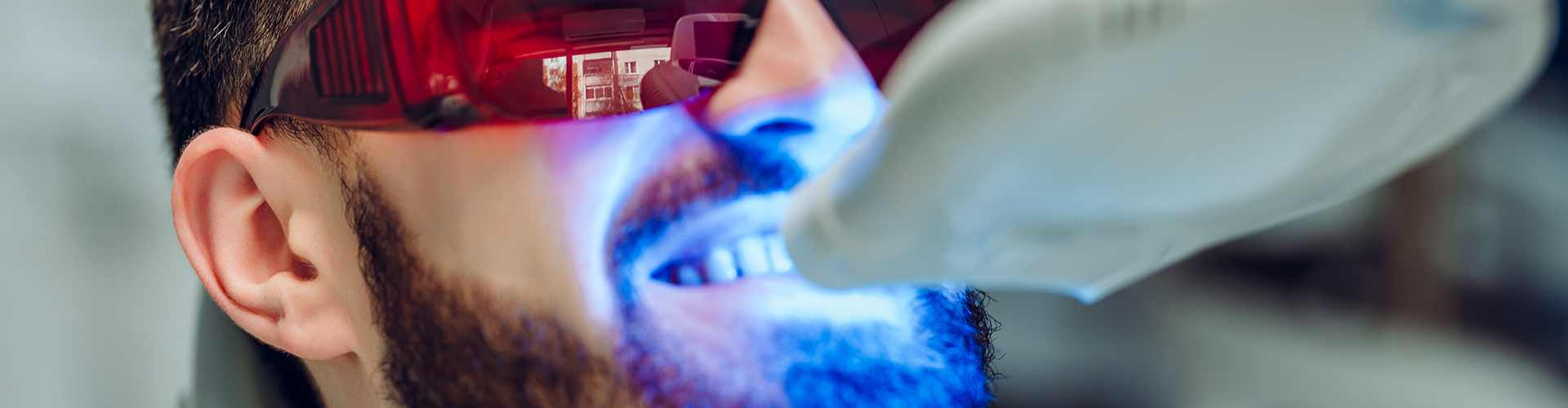 gloved hand shining blue light onto glasses-wearing man's smile
