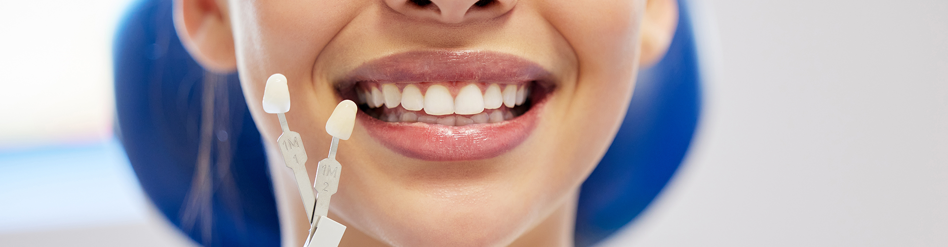 
gloved hands holding tooth shade-matching tool against woman's smile