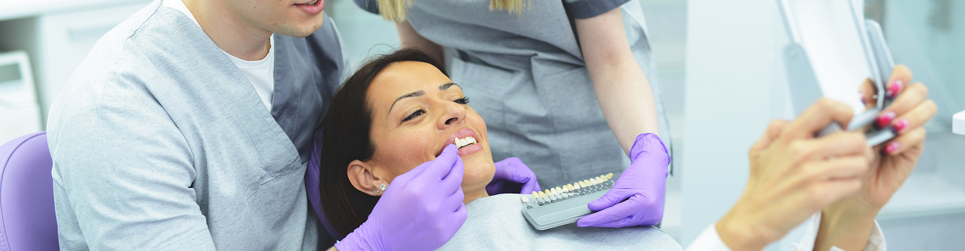 dentist and assistant holding tooth shade-matching tool against woman's teeth