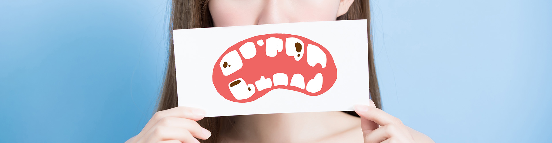 woman holding a drawing of a mouth with decayed teeth in front of her mouth