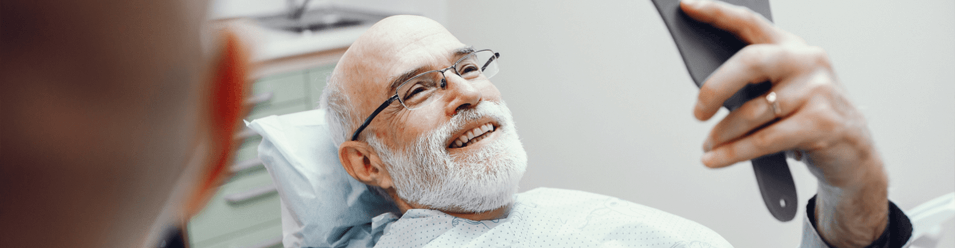 man in dentist chair holding a mirror and smiling