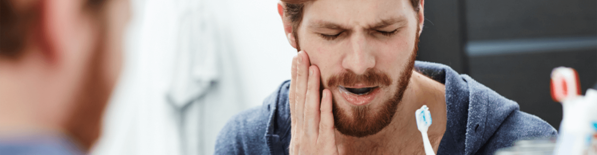man brushing his teeth with his hand on his face