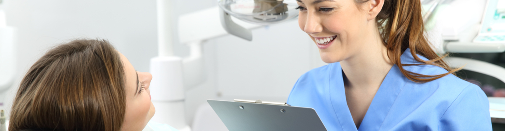 dentist holding a clip board and smiling at patient in chair