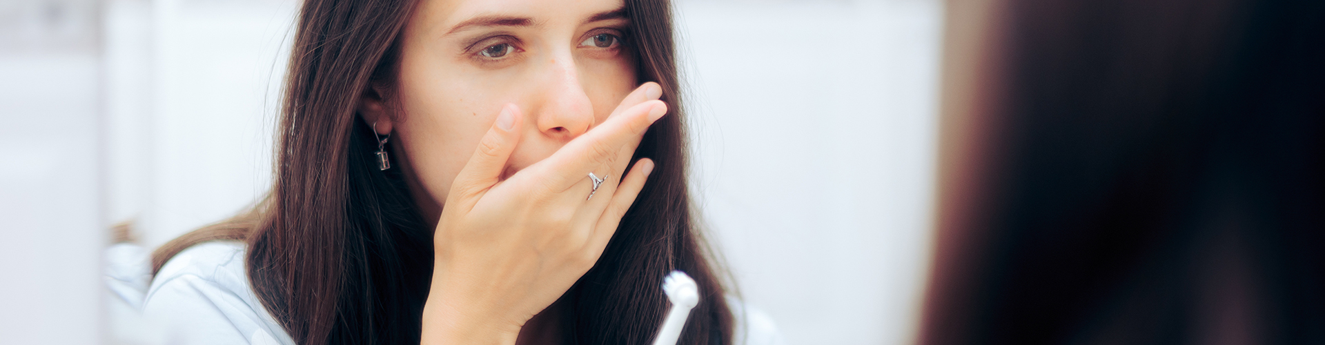 woman holding toothbrush covering her mouth