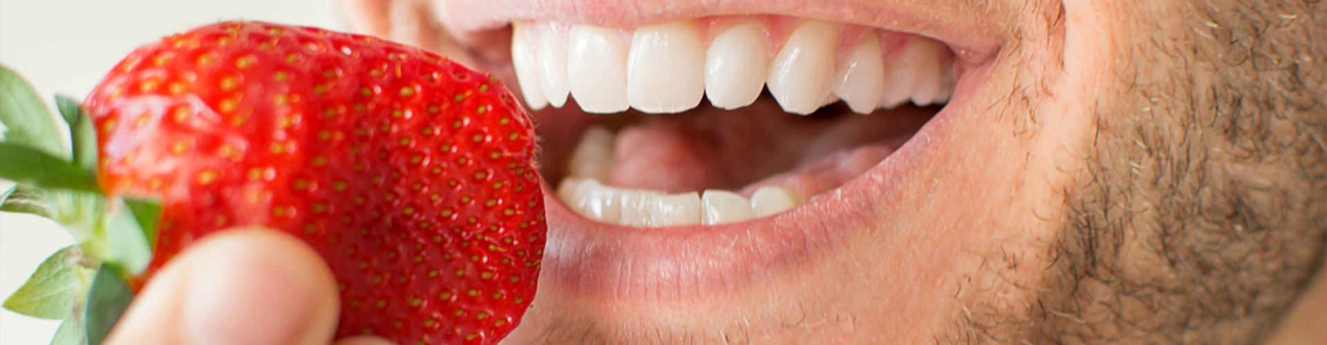 man holding a strawberry up to his mouth as he smiles 
