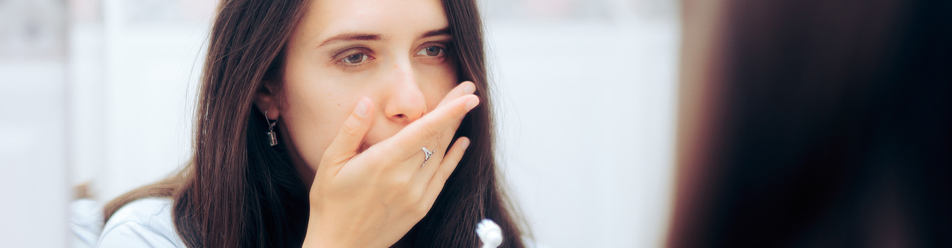 woman with toothbrush holding hand over mouth