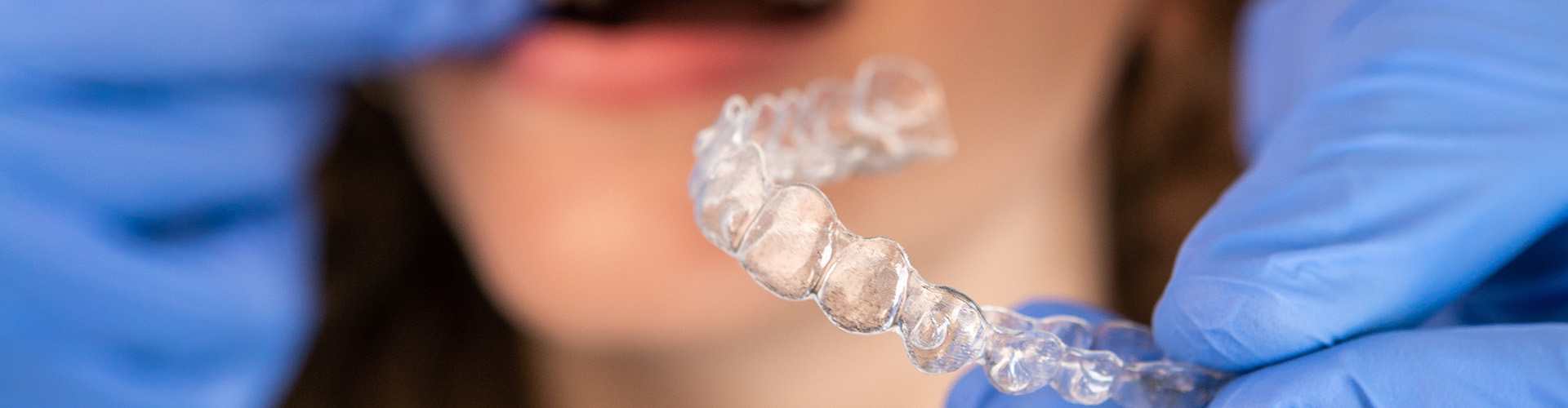 gloved hand holding clear aligner in front of woman