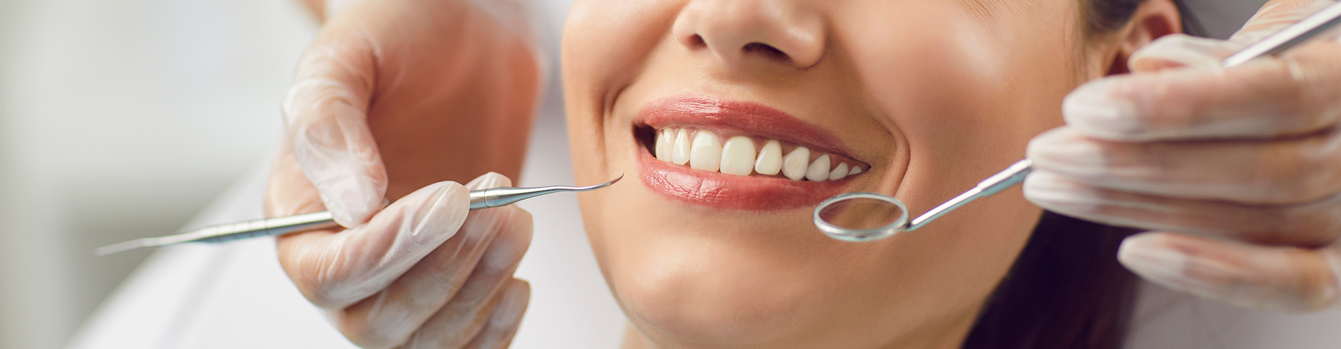 gloved hands holding dental tools beside smiling woman's mouth