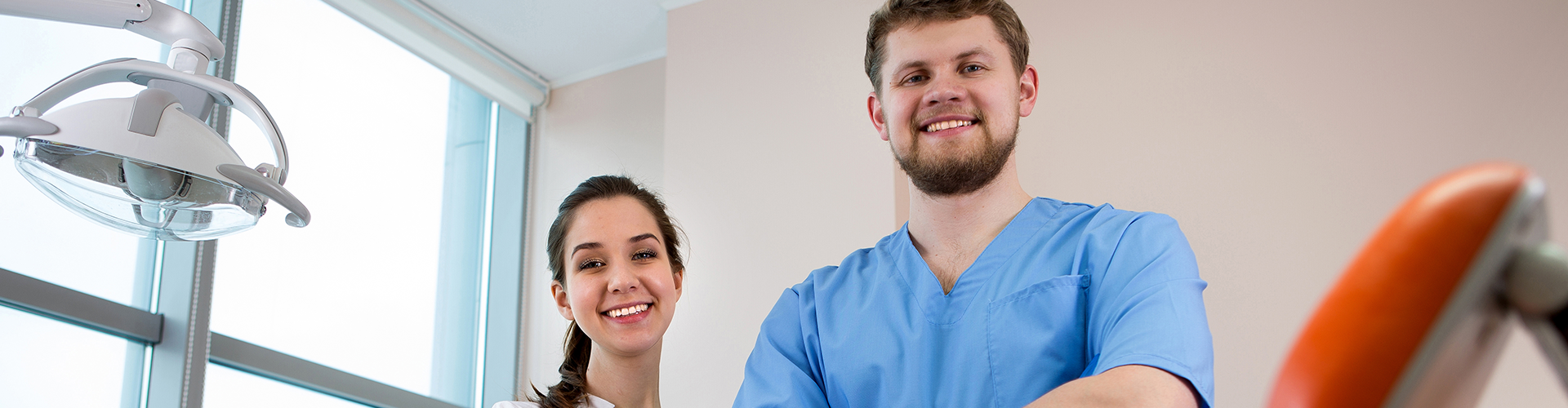 smiling man and woman wearing dental uniforms in dental office