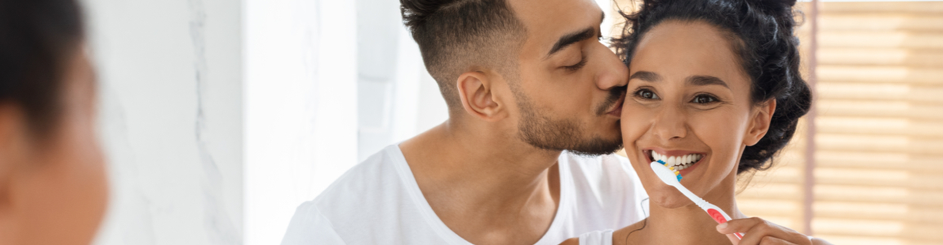 woman brushing teeth while man kisses cheek