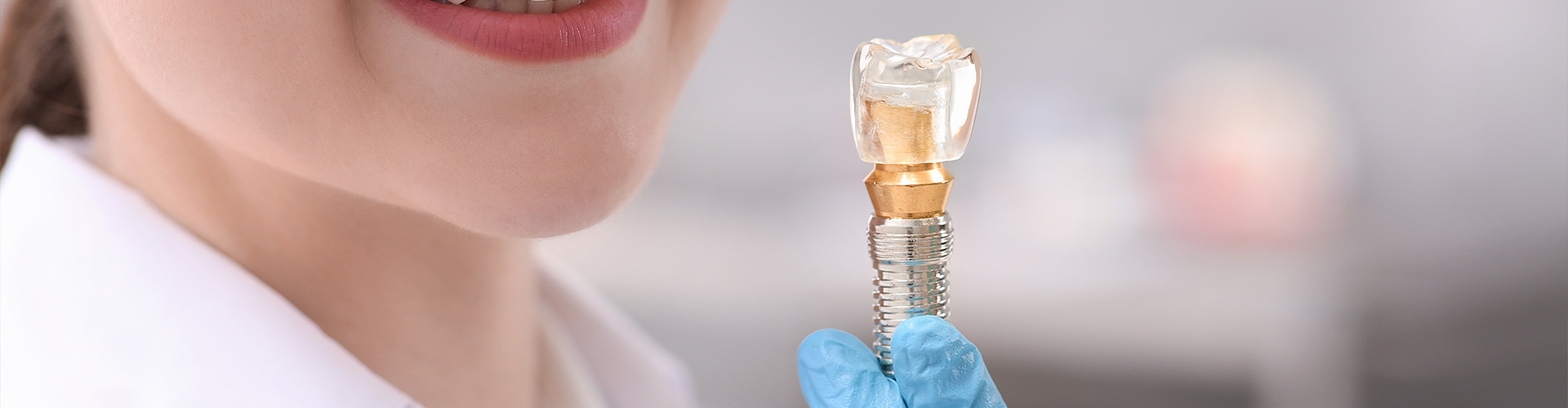 woman smiling at glass dental implant in gloved hand