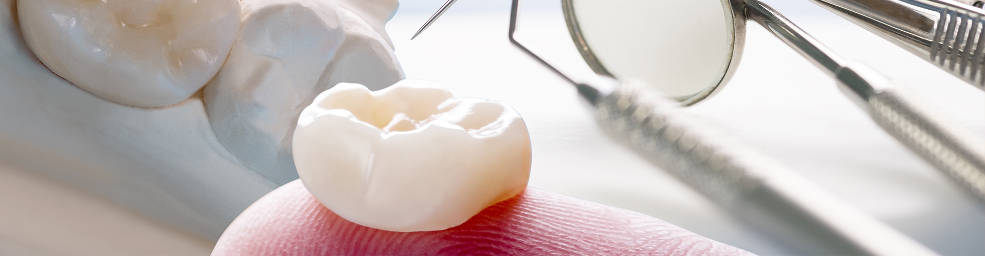 dental tools and a dental crown on a finger tip