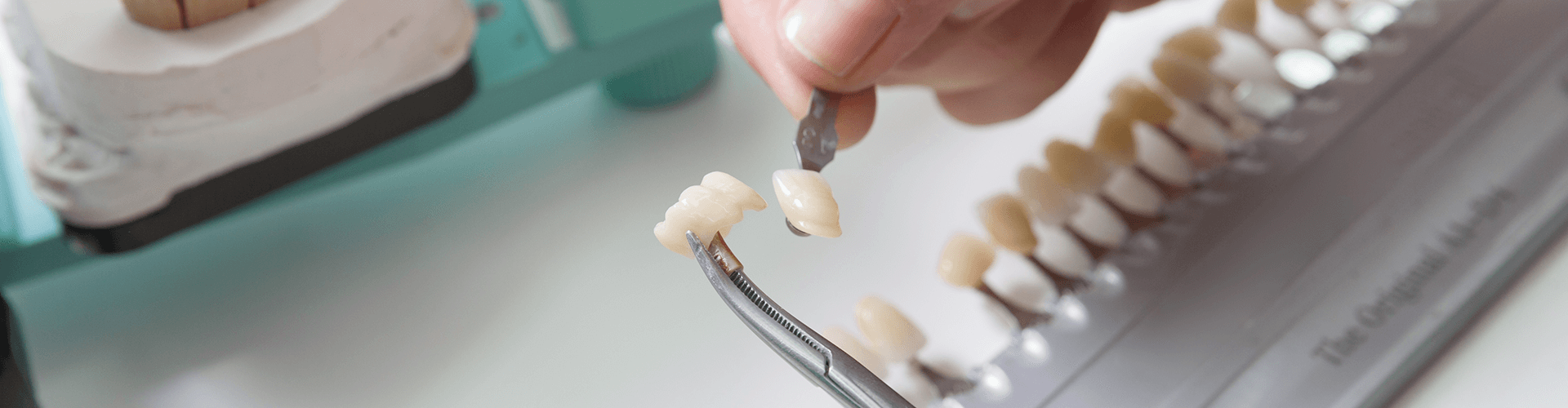 hands holding dental crowns and bridge in tweezers